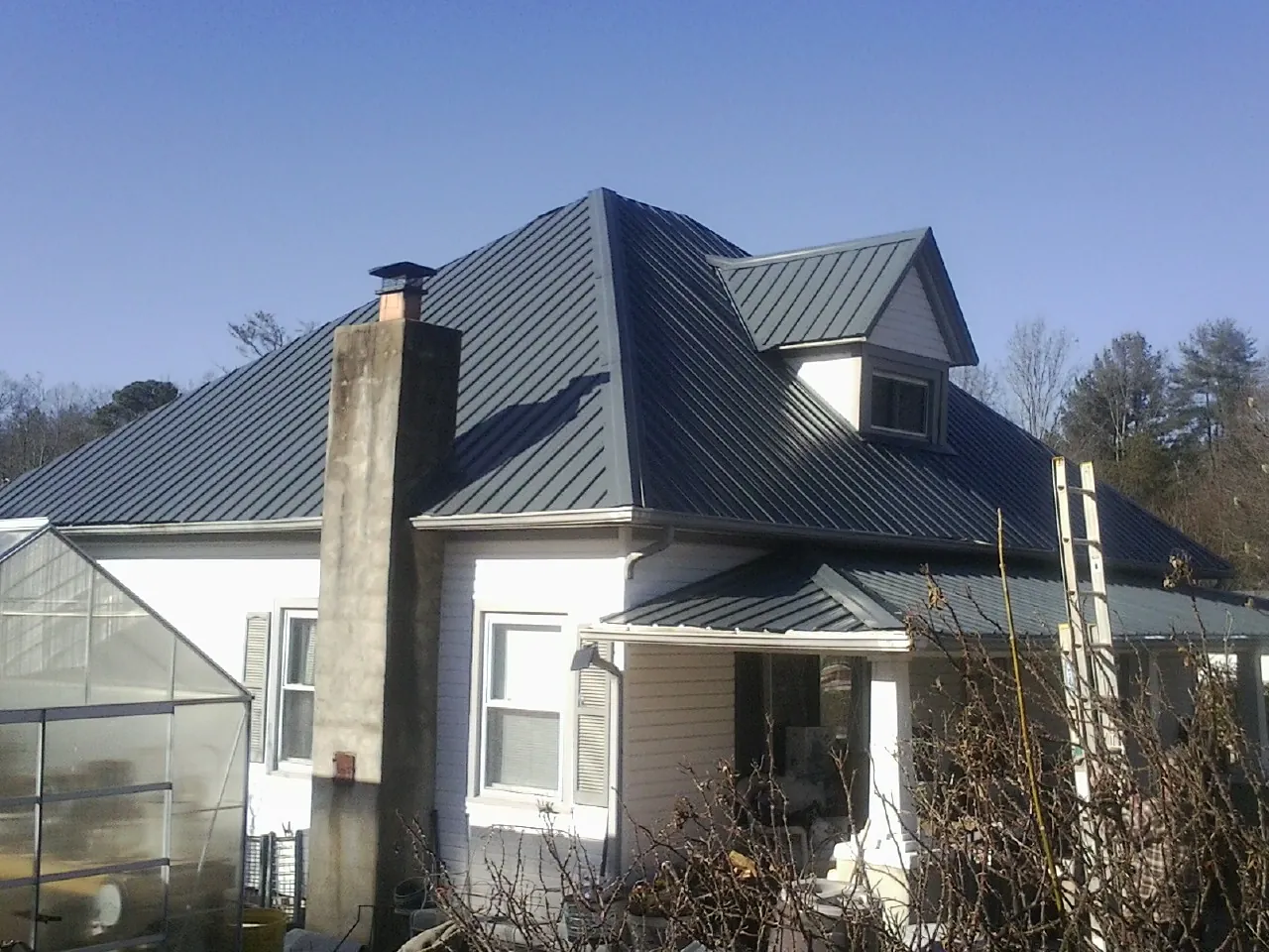 Dark blue standing seam metal roof on a white farmhouse with dormer — Slate & Tile Roof Repair by Roofing Brothers in Thor