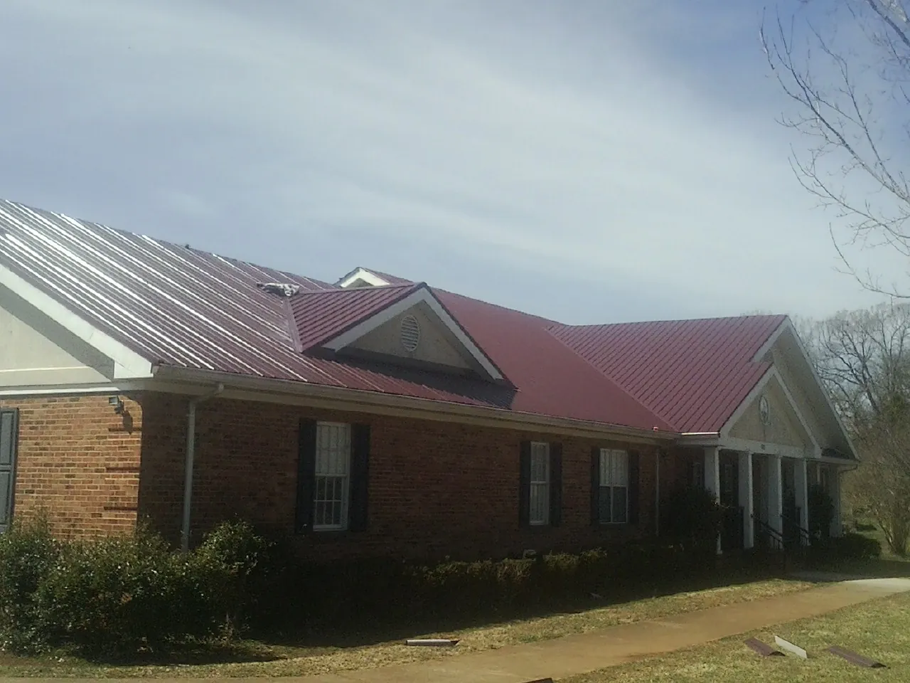 Red metal roof with gabled entries on a long brick building, from a Hail Damage Roof Repair job in Thor