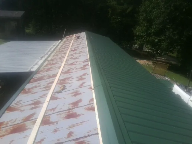 Old rusted panels beside newly installed green metal roofing — Wind Damage Roof Repair by Roofing Brothers in Thor