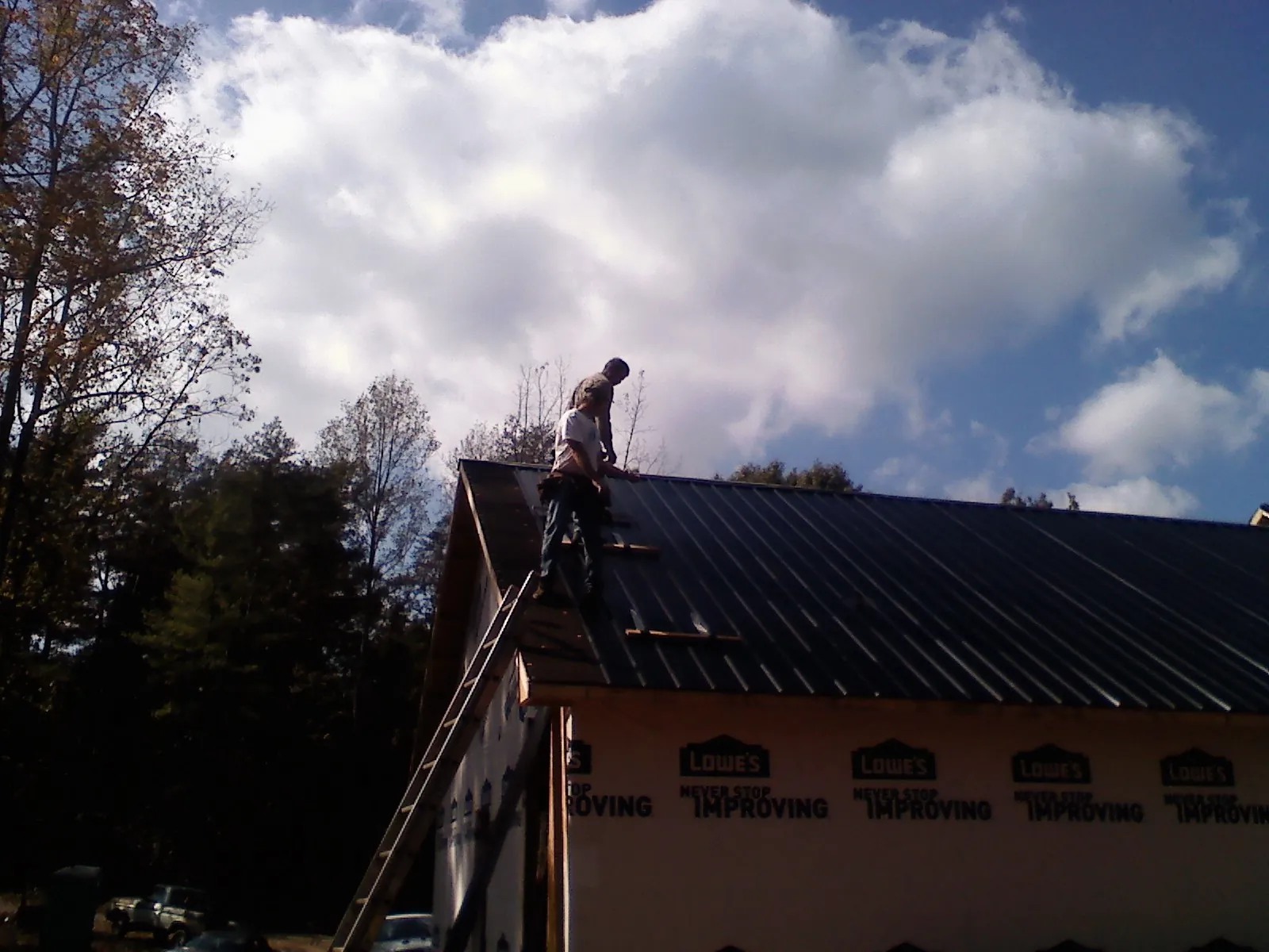Roofer fastening dark metal panels high against a cloudy sky, from a Roof Inspection job in Thor